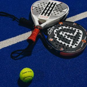 Collana padel Vibora acciaio Padel rackets and ball on blue textured court, highlighting equipment for the sport.